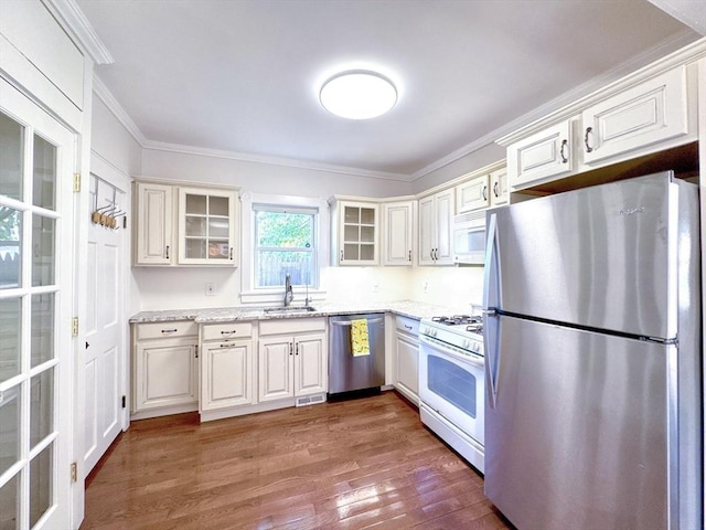 121 N Main St, Natick, MA 01760 - kitchen featuring stainless steel appliances, ornamental molding, wood finished floors, glass insert cabinets, and light stone counters