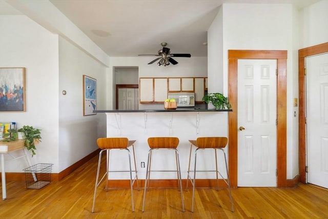 87 Bristol St Unit 3C, Cambridge, MA 02139 - kitchen with a breakfast bar, white microwave, a ceiling fan, and light wood-type flooring