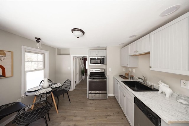 kitchen with light countertops, appliances with stainless steel finishes, white cabinets, a sink, and wood finished floors