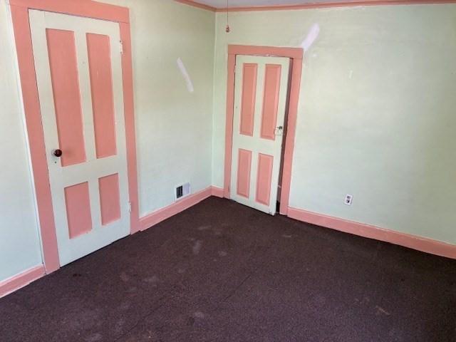 unfurnished room with dark colored carpet, visible vents, and baseboards