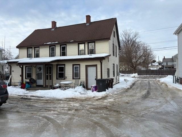 snow covered rear of property with a porch and a chimney