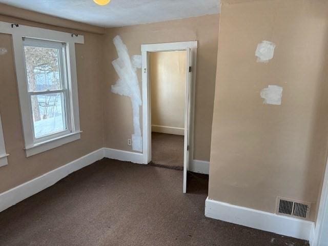 spare room with visible vents, baseboards, and dark colored carpet