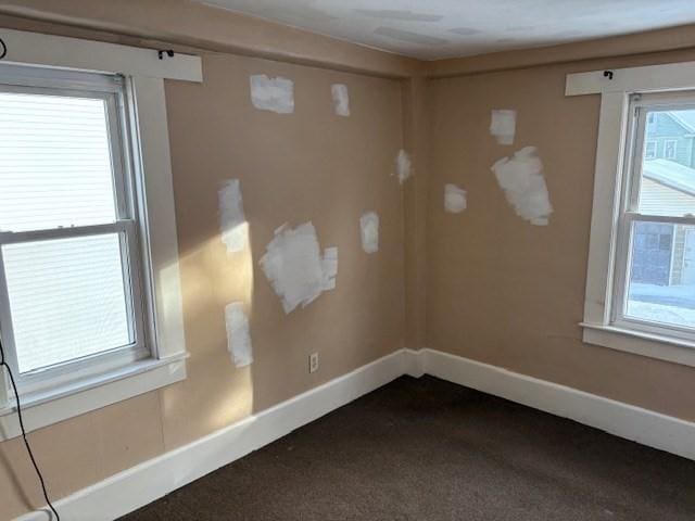 spare room featuring dark colored carpet and baseboards