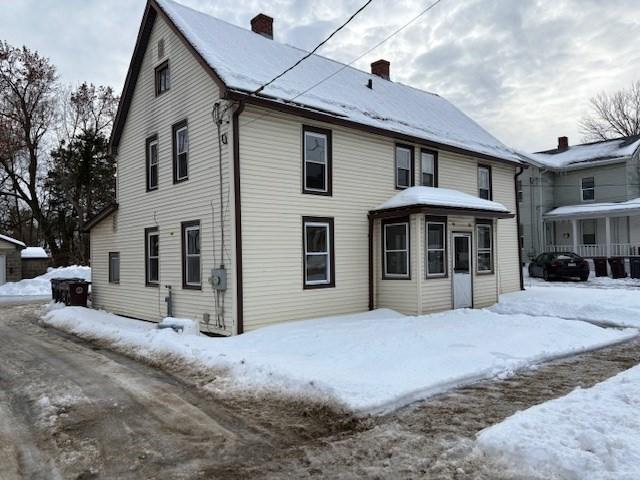 snow covered rear of property with a chimney