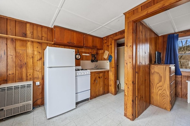 kitchen with white appliances, wooden walls, brown cabinets, light floors, and a sink