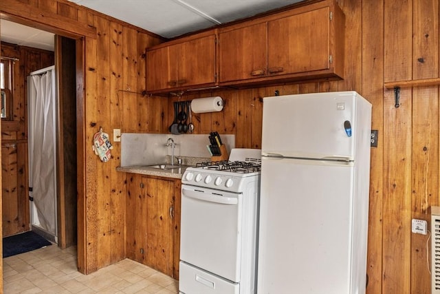 kitchen with white appliances, wood walls, a sink, and brown cabinets