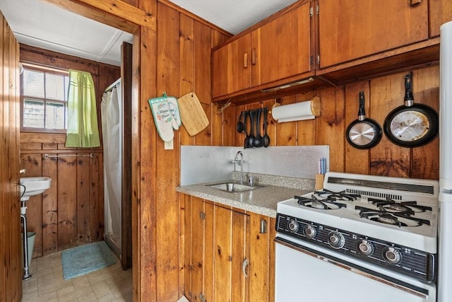 kitchen featuring wood walls, a sink, brown cabinetry, and white range with gas stovetop