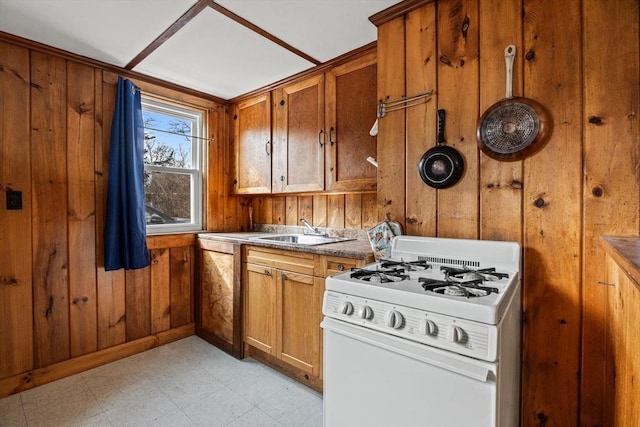 kitchen with light floors, brown cabinetry, a sink, wooden walls, and white gas range oven