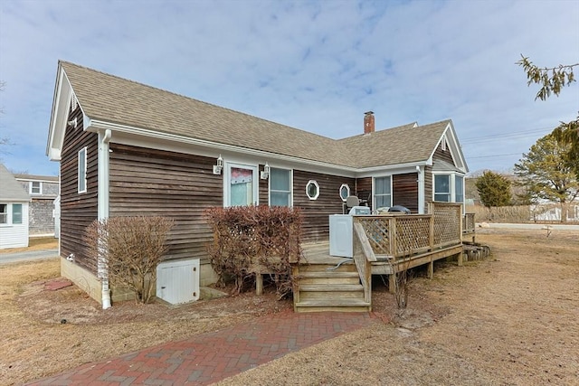 view of front of house with roof with shingles, a chimney, and a wooden deck