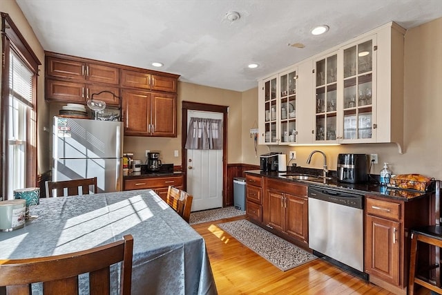 kitchen featuring light wood-type flooring, a sink, dark countertops, stainless steel appliances, and glass insert cabinets