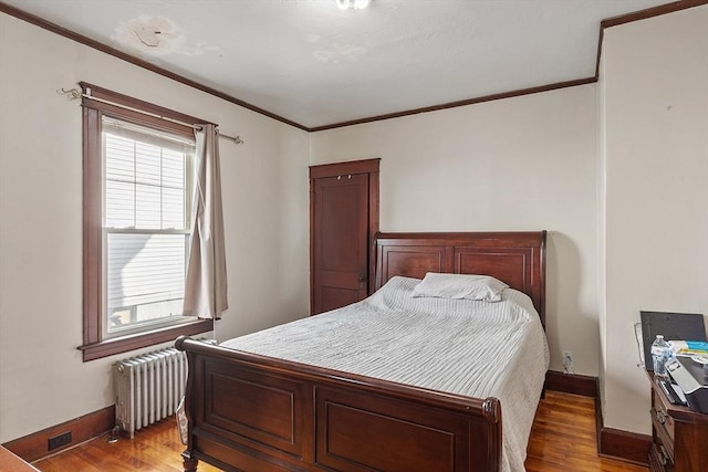 bedroom with crown molding, radiator heating unit, and wood finished floors