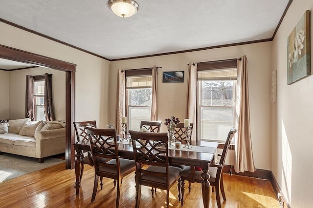 dining space featuring a textured ceiling, light wood-style floors, baseboards, and ornamental molding