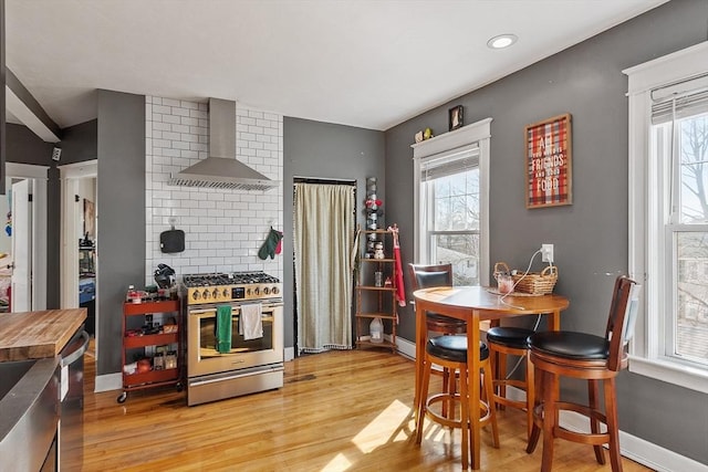 kitchen with a wealth of natural light, light wood finished floors, stainless steel range with gas stovetop, and wall chimney range hood