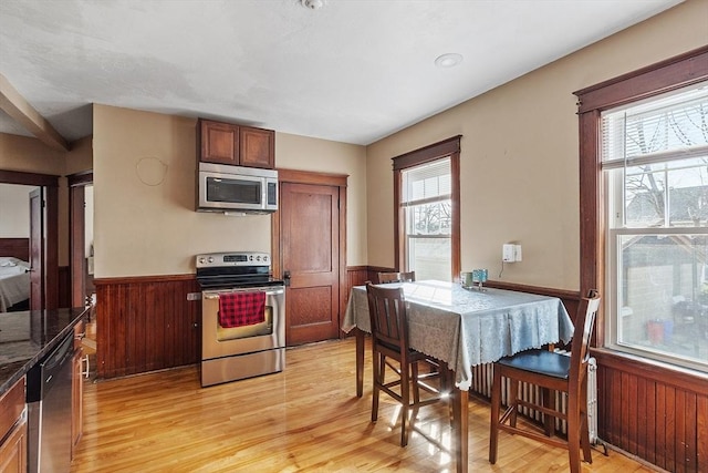 kitchen with a wainscoted wall, plenty of natural light, appliances with stainless steel finishes, and light wood-style floors