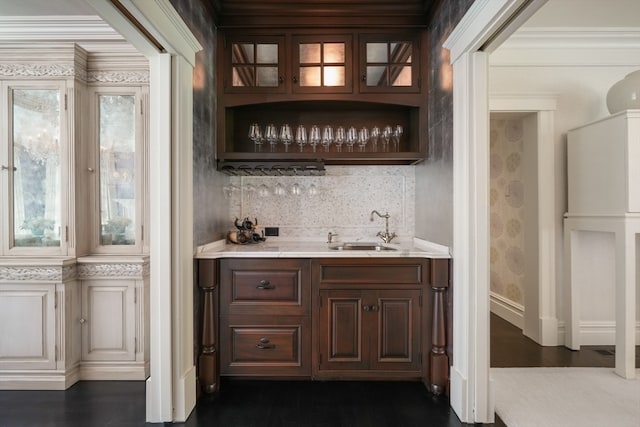 bar featuring dark wood-type flooring, crown molding, sink, and backsplash