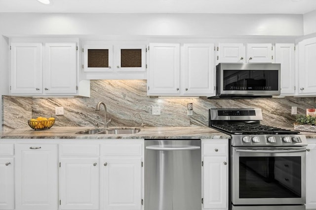 kitchen with light stone countertops, a sink, stainless steel appliances, white cabinets, and tasteful backsplash