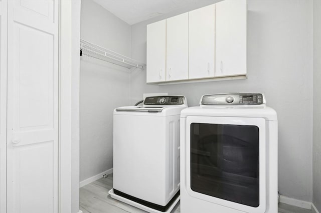 laundry room featuring light wood-style flooring, cabinet space, baseboards, and washer and clothes dryer