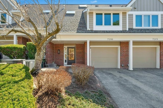 multi unit property with brick siding, an attached garage, driveway, and roof with shingles