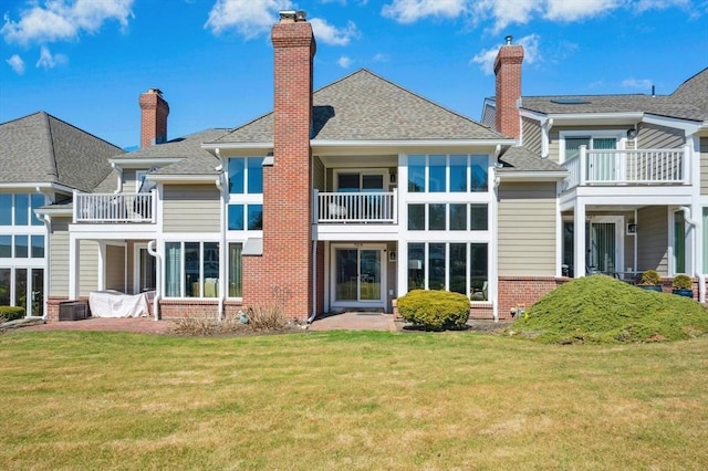 rear view of property with a yard, brick siding, roof with shingles, and a chimney