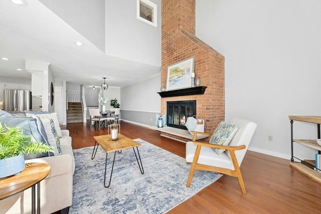 living room with a fireplace, wood finished floors, baseboards, and a towering ceiling