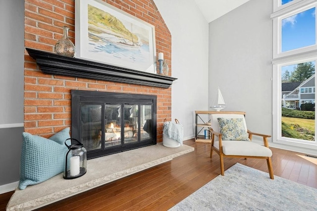 sitting room featuring vaulted ceiling, a brick fireplace, baseboards, and hardwood / wood-style flooring