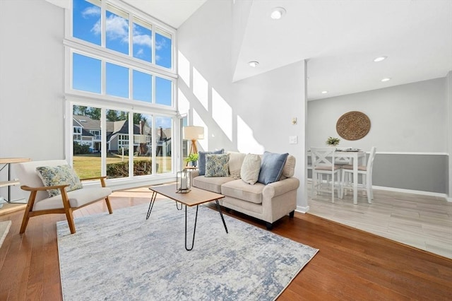 living room with a towering ceiling, recessed lighting, baseboards, and wood finished floors