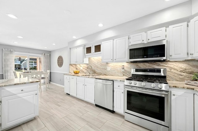 kitchen with light stone countertops, a sink, stainless steel appliances, white cabinetry, and tasteful backsplash