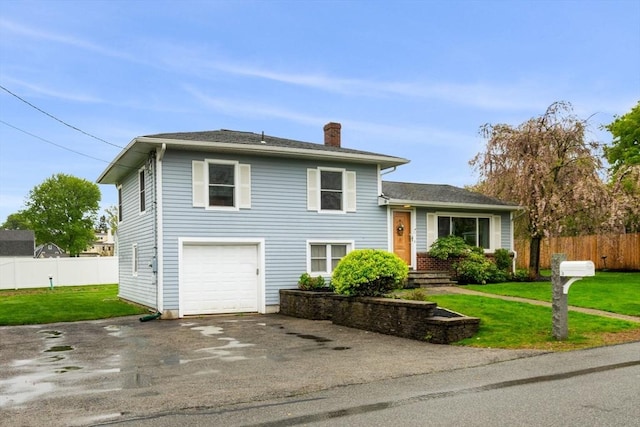 split level home with a chimney, driveway, a front lawn, and fence