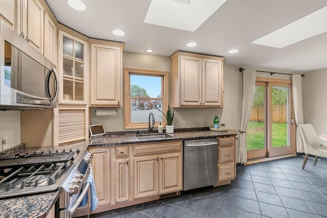 kitchen with appliances with stainless steel finishes, glass insert cabinets, a skylight, and a sink