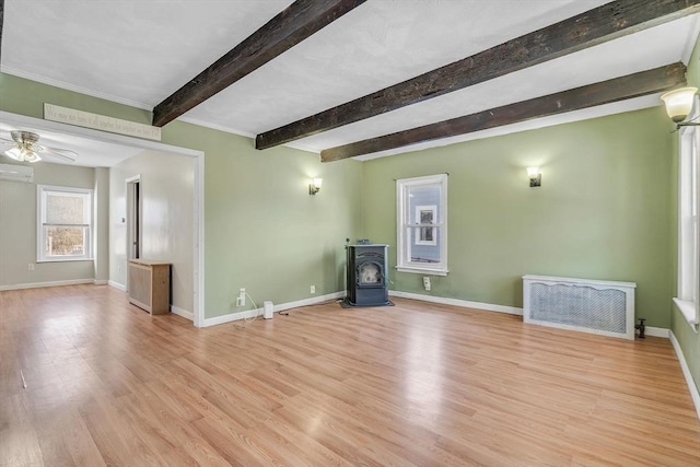 unfurnished living room featuring ceiling fan, wood finished floors, baseboards, beam ceiling, and a wood stove