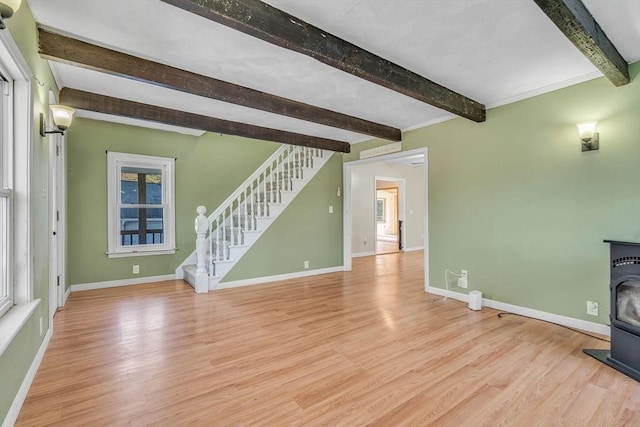 unfurnished living room featuring a wood stove, wood finished floors, beamed ceiling, baseboards, and stairs