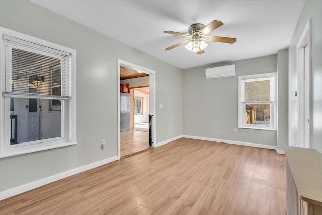 spare room featuring baseboards, ceiling fan, a wall mounted AC, and light wood-style floors