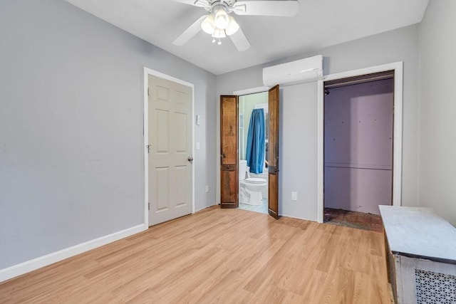 unfurnished bedroom featuring a wall unit AC, a ceiling fan, ensuite bath, light wood-type flooring, and baseboards