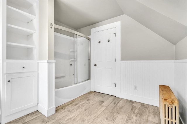 bathroom featuring a wainscoted wall, radiator heating unit, wood finished floors, and lofted ceiling