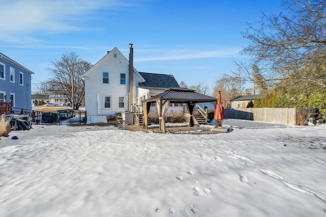 snow covered back of property with fence and a gazebo