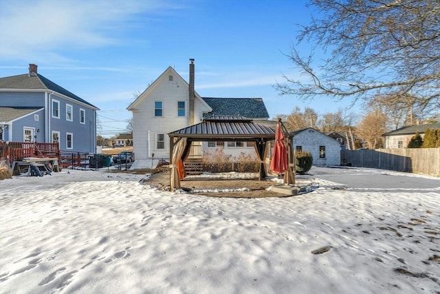 snow covered back of property with metal roof, an outbuilding, a standing seam roof, fence, and a gazebo