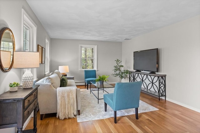 living area featuring baseboards, baseboard heating, wood finished floors, and visible vents