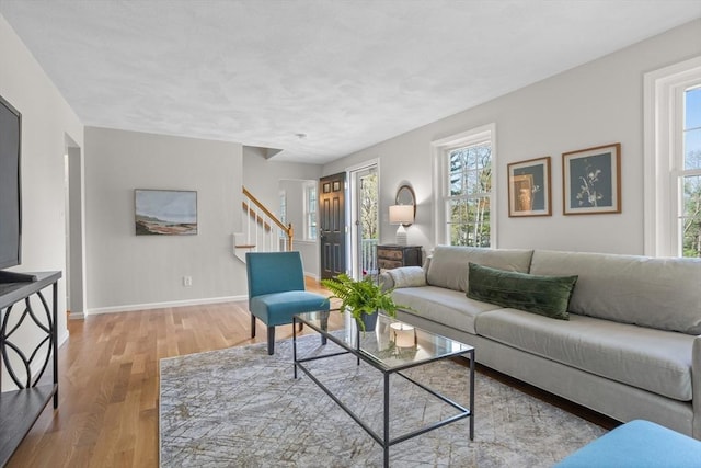 living area with baseboards, wood finished floors, a healthy amount of sunlight, and stairway