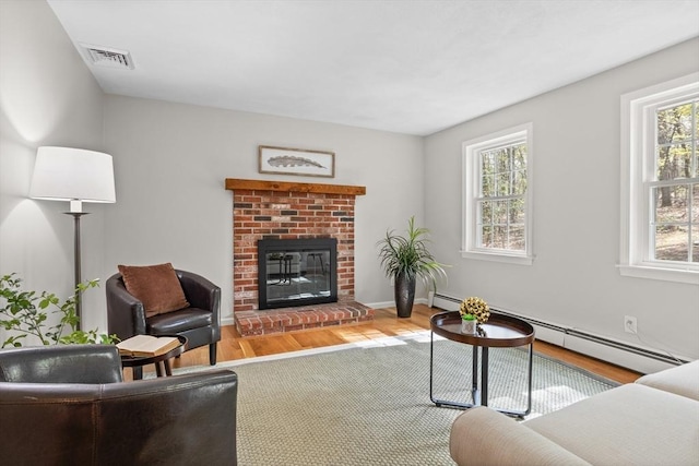 living room featuring a brick fireplace, a baseboard heating unit, wood finished floors, and visible vents