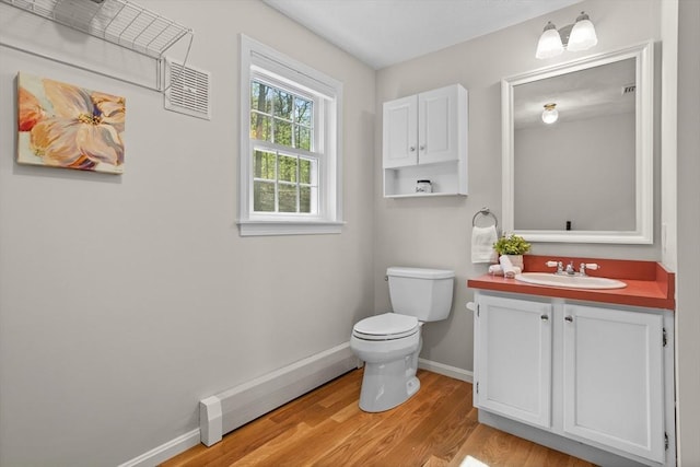 bathroom featuring visible vents, vanity, wood finished floors, toilet, and a baseboard heating unit