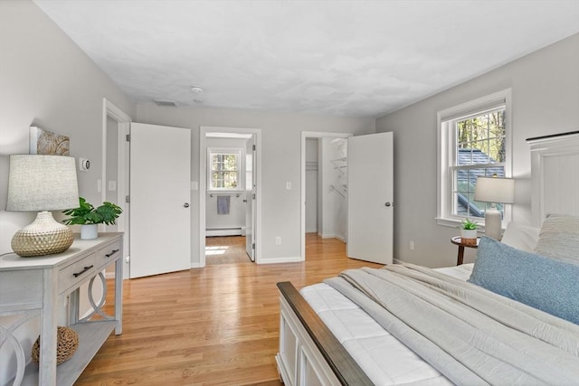 bedroom featuring visible vents, light wood-style floors, baseboards, a walk in closet, and a baseboard radiator