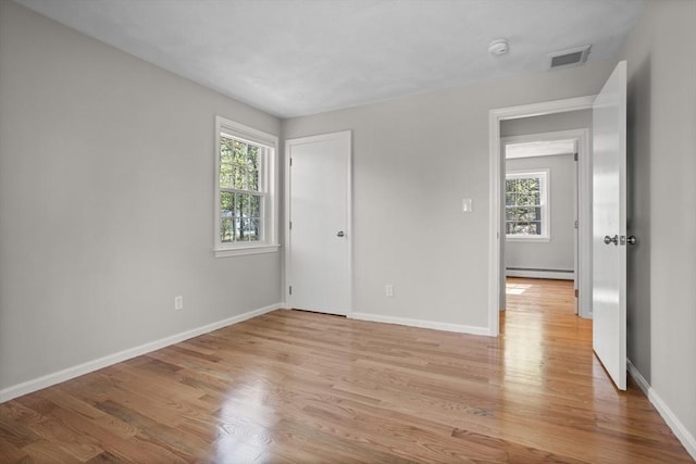 unfurnished bedroom with baseboards, baseboard heating, light wood finished floors, and visible vents