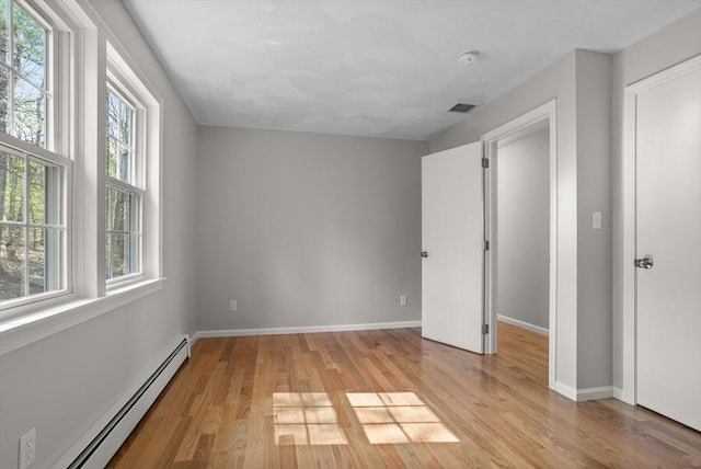 unfurnished bedroom featuring baseboards, visible vents, baseboard heating, and light wood-type flooring