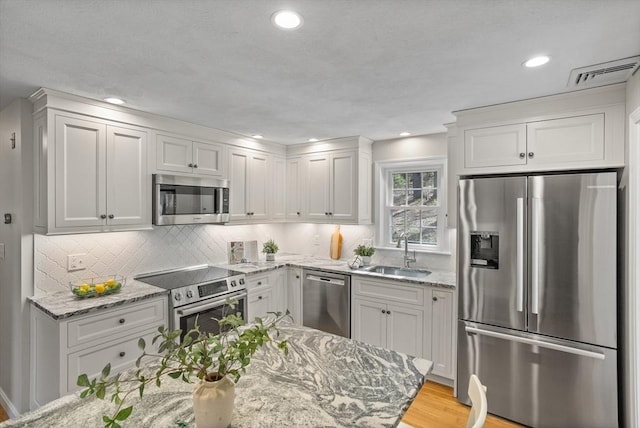 kitchen featuring appliances with stainless steel finishes, light stone counters, a sink, backsplash, and visible vents