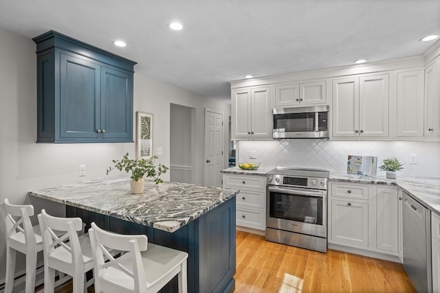 kitchen featuring light stone counters, light wood-style floors, a breakfast bar area, stainless steel appliances, and tasteful backsplash