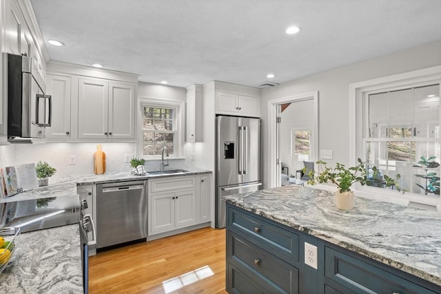 kitchen with backsplash, white cabinetry, a sink, stainless steel appliances, and light wood-style flooring