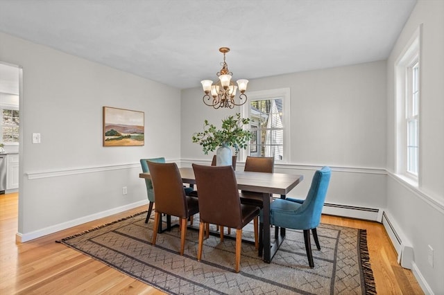 dining space featuring a baseboard heating unit, baseboards, an inviting chandelier, and light wood-style floors