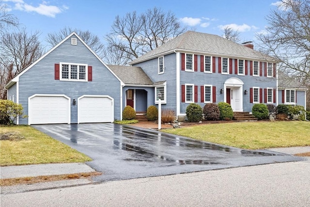 view of front of property featuring roof with shingles, a chimney, a front lawn, a garage, and aphalt driveway