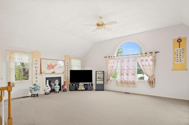 living room featuring lofted ceiling, ceiling fan, carpet flooring, a glass covered fireplace, and baseboards