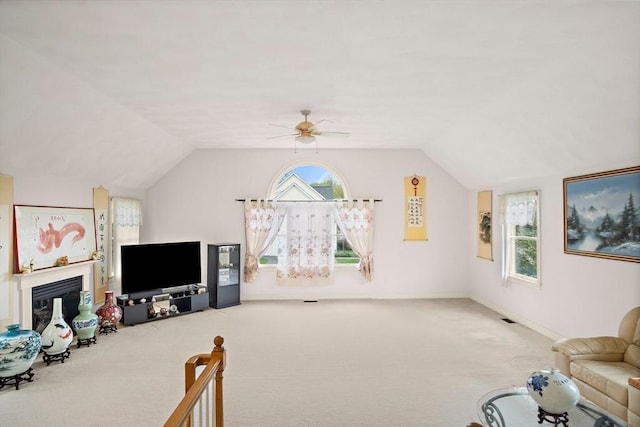 unfurnished living room featuring carpet flooring, vaulted ceiling, ceiling fan, a glass covered fireplace, and baseboards